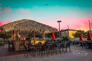 Outdoor dining area with a thatched-roof bar and tables under shade.