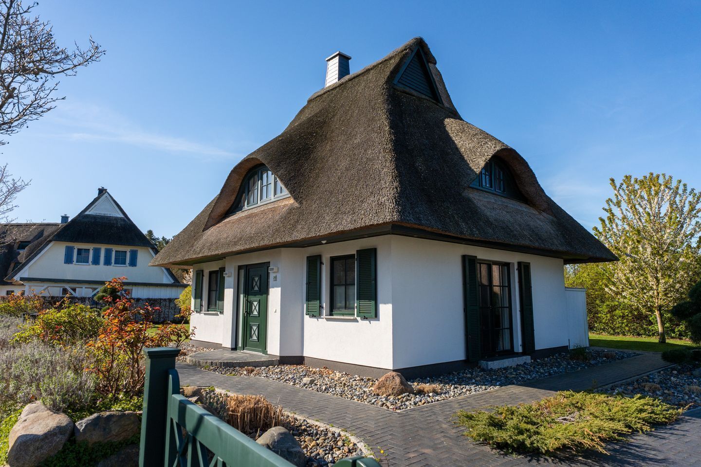 Ein traditionelles Haus mit strohgedecktem Dach, weißer Fassade, einer grünen Tür und einer kleinen Veranda.