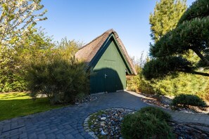 A building with a green door and a thatched roof, surrounded by trees and a paved pathway. - Vacation home Seeadler 49 - Holiday home Seeadler 49 - Close to nature (Fuhlendorf)