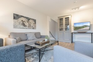Una sala de estar moderna con un sofá gris, una mesa de centro de vidrio y un televisor sobre un mueble.