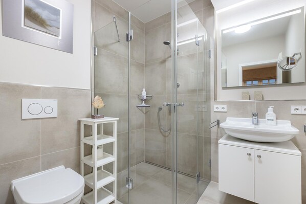 Une salle de bain moderne avec une douche à parois de verre, un lavabo blanc et des toilettes.