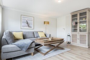 A modern living room with a grey sofa, a wooden coffee table, a lamp, and a cabinet with glass doors.