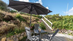 Eine Terrasse mit Tisch und Stühlen, einem großen Sonnenschirm und einer Treppe, die einen Hügel hinaufführt.