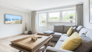 Ein modernes Wohnzimmer mit einer Couch, einem Holztisch, einem Fernseher und einem Fenster mit Vorhängen.
