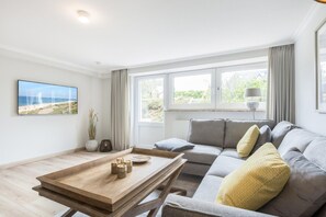 Ein modernes Wohnzimmer mit einer Couch, einem Holztisch, einem Fernseher und einem Fenster mit Vorhängen.
