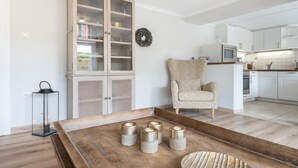 Eine moderne Küche mit weißen Schränken, einem Holzschrank mit Glastüren, einem Korbstuhl und einem Holztisch mit Kerzen.