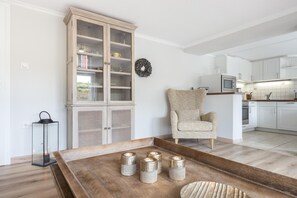 Eine moderne Küche mit weißen Schränken, einem Holzschrank mit Glastüren, einem Korbstuhl und einem Holztisch mit Kerzen.