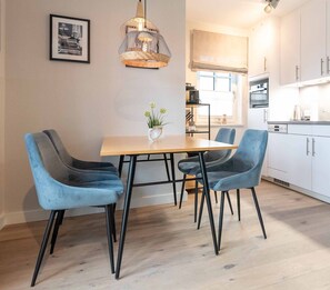A dining area with a wooden table and four blue chairs, a hanging light fixture, and a framed picture on the wall.