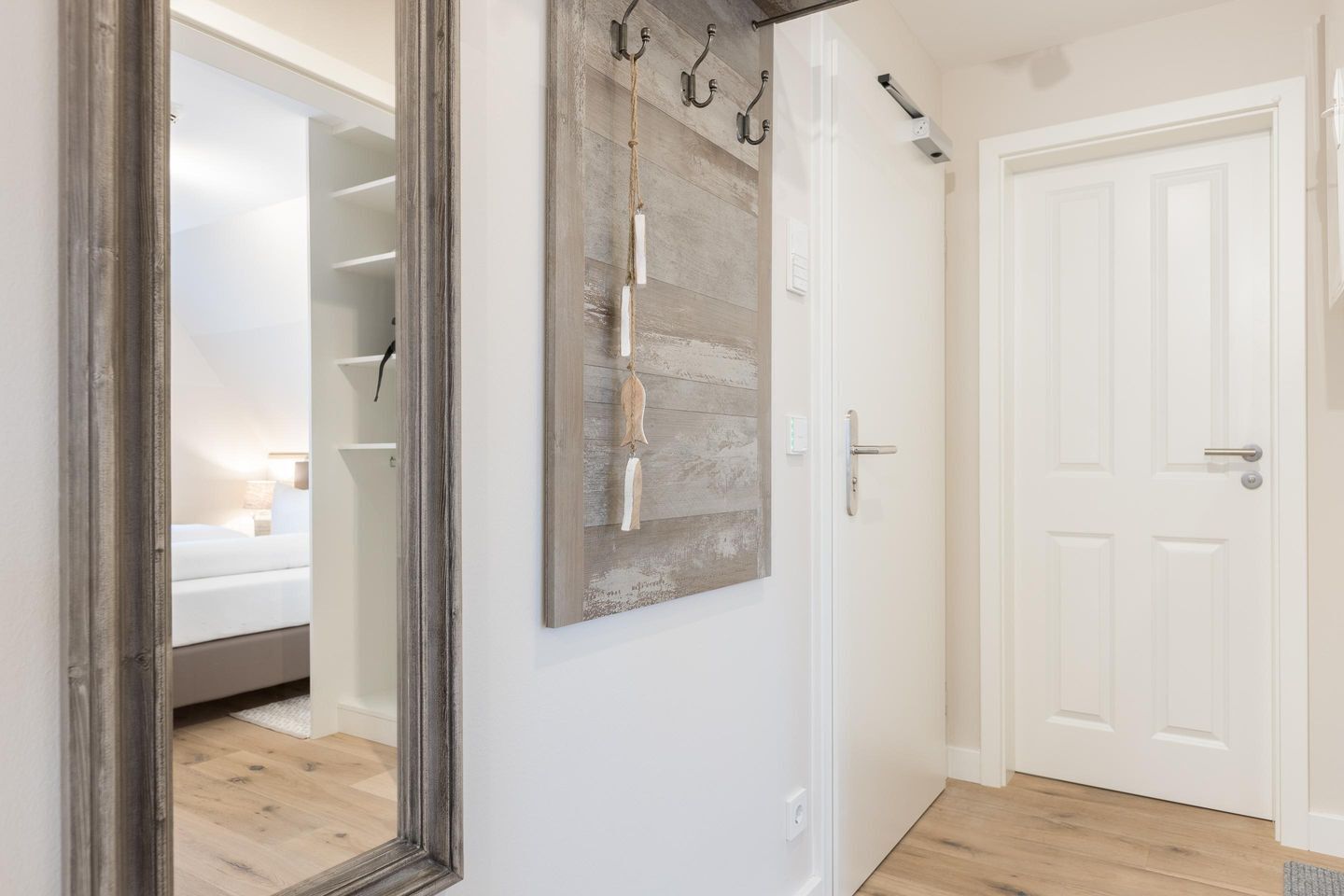 A hallway with a mirror, a rustic wall art piece, and a white door.