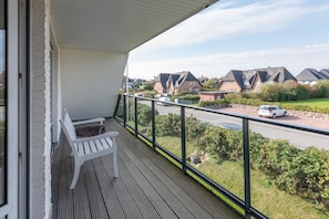 A balcony with a white bench, a view of a street with houses, and a clear sky.
