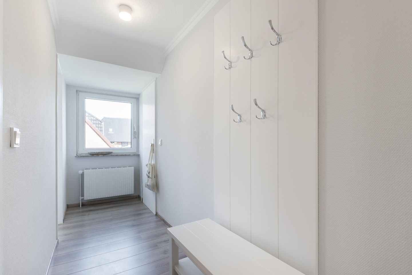 A hallway with a white bench, a radiator, and a window with a view of buildings.