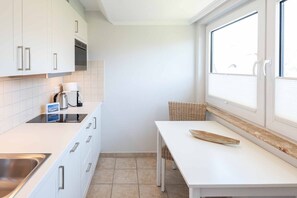 Una cocina compacta con armarios blancos, estufa integrada, lavamanos y ventana con persianas.
