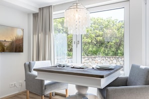 Un comedor con una mesa dispuesta para dos, una araña y vistas al exterior con vegetación.