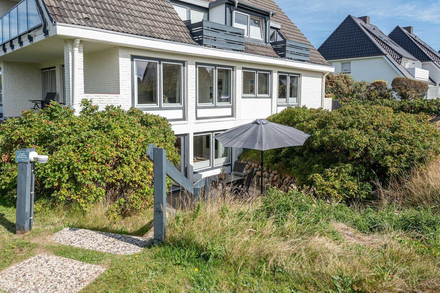 Une maison moderne à deux étages, dotée d’un grand balcon et d’un espace extérieur aménagé et abrité.