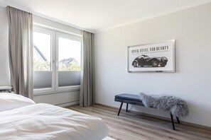 Una camera d'hotel con un'ampia finestra, un letto, una panca con una coperta soffice e un quadro appeso al muro.