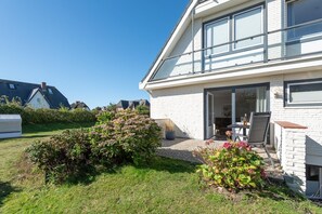 Una casa moderna con un'ampia vetrata, un patio con mobili da esterno e un giardino curato.