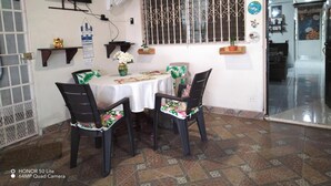 Zona pranzo con tavolo rotondo, quattro sedie, TV a parete, una ventola decorativa e una finestra con grate ornamentali.