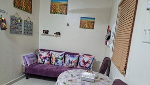 Un ambiente accogliente con un divano viola, un tavolino con una tovaglia floreale e opere d'arte raffiguranti girasoli e paesaggi.