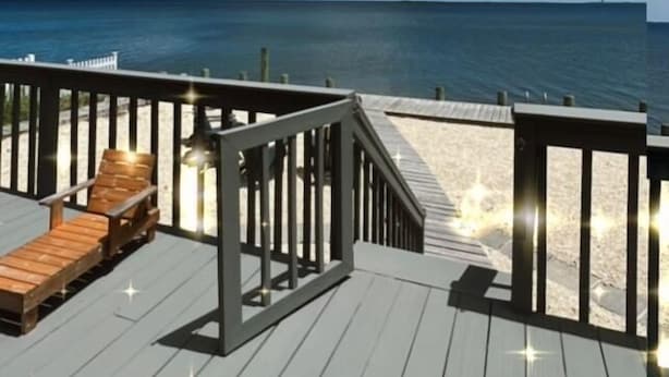 A wooden deck with a railing, a wooden lounge chair, and a view of the ocean.