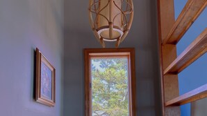A room with a large window, a wooden ceiling light, a framed picture, and a white teddy bear.