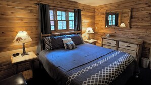A cozy log cabin bedroom with a large bed, two bedside tables with lamps, a dresser, and a window with curtains. - On The River, Hot Tub, Walk to Town #6002 (Estes Park)