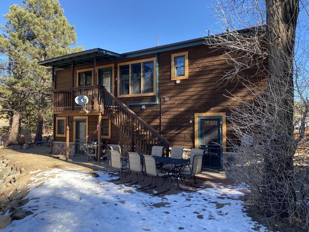 A two-story wooden cabin with a balcony, outdoor seating, and a fireplace.