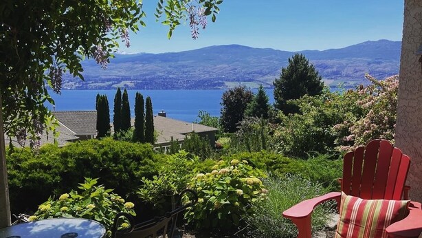 A covered patio with a table and chairs, a red Adirondack chair, and a view of a lake and mountains.