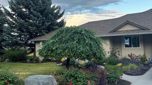 A residential house with a well-maintained garden, including a large rock, various plants, and a lawn.