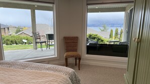 A bedroom with a large bed, a chair, and a view of a balcony and outside scenery.