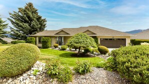 A single-story house with a well-maintained lawn, a large coniferous tree, and a garage.