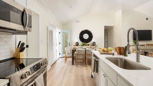 A modern kitchen with a stainless steel stove, a microwave, and a large sink. There is a dining area with a table and chairs, and a large mirror on the wall. - Sawyer by AvantStay | Stunning Isle Of Palms Home w/ Pool! (Isle Of Palms)