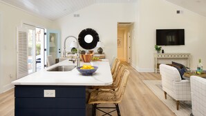 A modern kitchen with a central island, built-in appliances, and a dining area with wicker chairs. - Sawyer by AvantStay | Stunning Isle Of Palms Home w/ Pool! (Isle Of Palms)