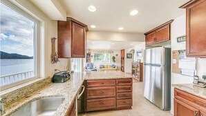 Una cocina con encimeras de granito, armarios de madera, un refrigerador de acero inoxidable y vistas a un lago.