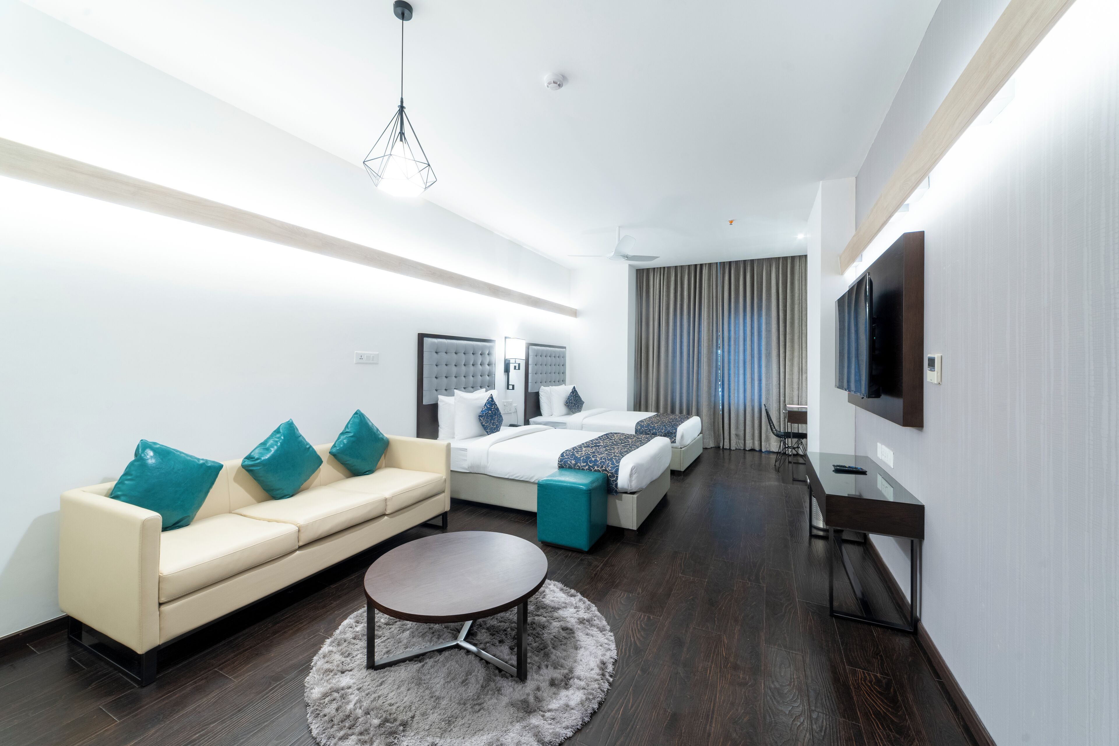 Una habitación de hotel moderna con sofá, dos camas, televisor y escritorio.