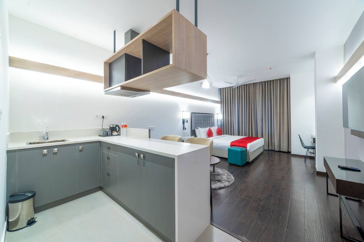 Una habitación de hotel moderna con cocina, cama con detalles en rojo, escritorio y una silla.