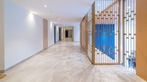 Un couloir doté d’un sol carrelé, d’une cloison en bois ornée d’un motif géométrique et d’un mur d’accent bleu.