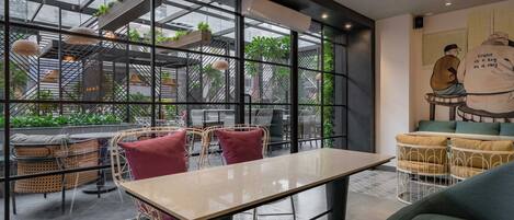 A modern cafe with a glass wall, wicker furniture, and a mural.