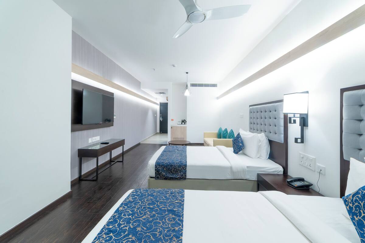 Habitación de hotel con dos camas, un escritorio, un televisor de pantalla plana, un ventilador de techo y una mesita de noche con teléfono.