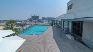 Une piscine sur le toit offrant une vue sur la ville, une terrasse en bois et une architecture moderne.
