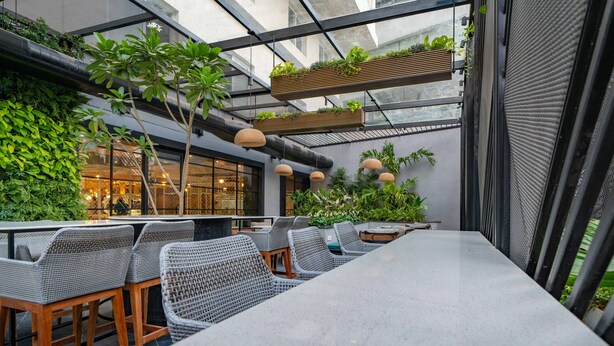 Un espace de restauration intérieur avec une longue table, des chaises en osier et des plantes suspendues.