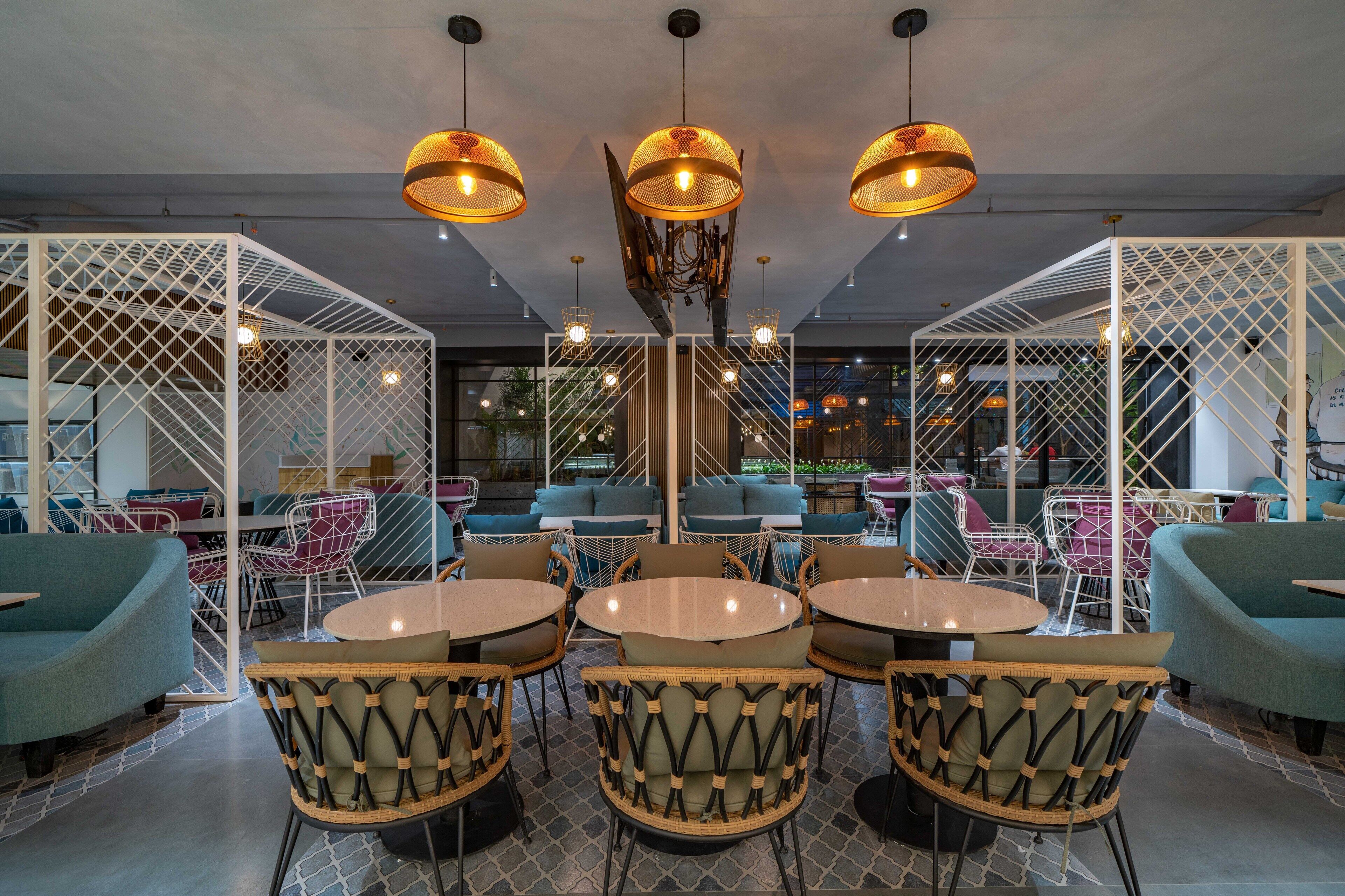 A modern interior with round tables and wicker chairs, white partitions, and hanging pendant lights.