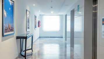 Um corredor moderno com piso de mármore polido, obras de arte nas paredes e um elevador à direita.