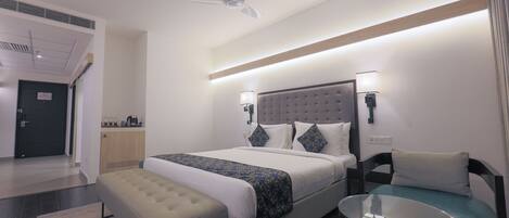 A modern hotel room with a large bed, a small table, a bench, and a ceiling fan.