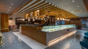 Un restaurant moderne doté d’un comptoir central où sont présentés les desserts, de lambris en bois et d’un éclairage suspendu.