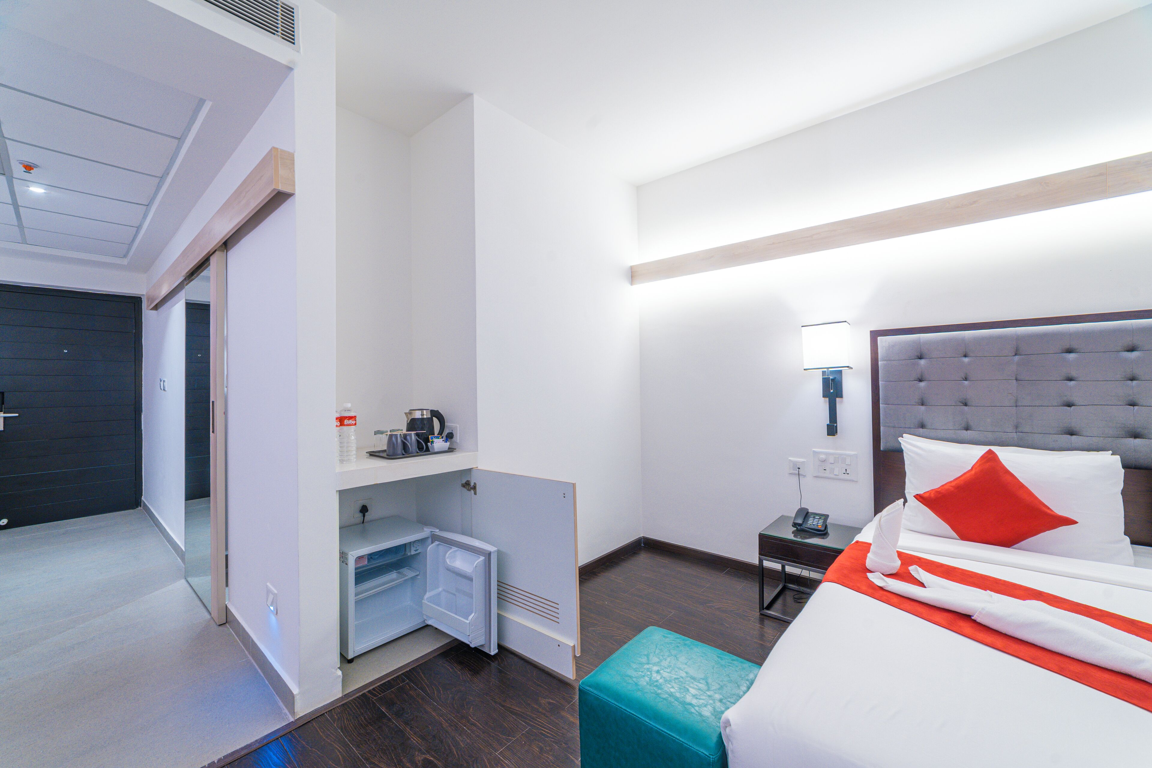 Une chambre d’hôtel comprenant un lit, une table de chevet, une petite table, un mini-réfrigérateur et un banc intégré.
