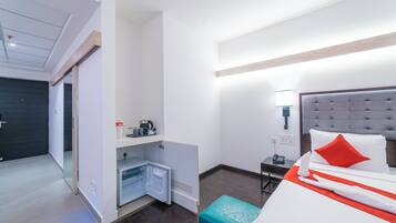 Une chambre d’hôtel comprenant un lit, une table de chevet, une petite table, un mini-réfrigérateur et un banc intégré.