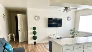 A modern living room with a dark blue sofa, a marble kitchen island, a flat-screen TV, and decorative wall art. - Spacious comfort, 1st FL, parking, 2 TVs, laundry,Beautiful views of NYC skyline (Clifton)