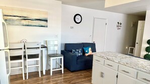 A modern kitchen with white cabinets, a dark blue sofa, and a dining area with white chairs. - Spacious comfort, 1st FL, parking, 2 TVs, laundry,Beautiful views of NYC skyline (Clifton)