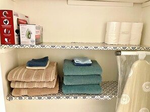 A bathroom with a shower curtain, a towel rack with folded towels, and boxes of toiletries on shelves. - Spacious comfort, 1st FL, parking, 2 TVs, laundry,Beautiful views of NYC skyline (Clifton)