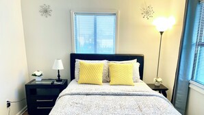 A bedroom with a bed, two nightstands, a lamp, and a window with blinds. - Spacious comfort, 1st FL, parking, 2 TVs, laundry,Beautiful views of NYC skyline (Clifton)